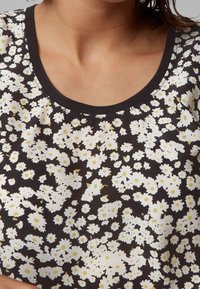 Květinový top s černým pozadím, zdobený bílými květinami a žlutými akcenty, s kulatým výstřihem, měkkou textilií a krátkými rukávy.