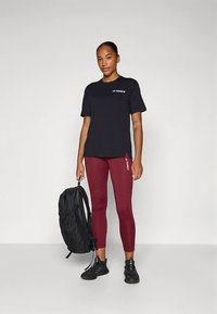 Črna majica s simbolom "Terrex", burgundske legice z logotipnimi poudarki, črni športni copati in črna nahrbtnik. Gladke teksture in prilegajoča zasnova.