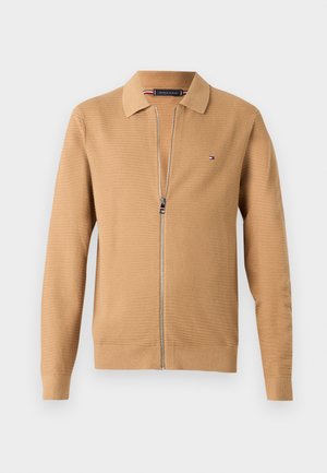 Tan zip-up cardigan with a textured knit, collar, and long sleeves. Features a logo on the left chest and a smooth zipper closure.