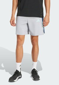 Shorts de sport gris clair en matériau synthétique, avec un logo Adidas en aqua et des accents noirs sur les côtés.