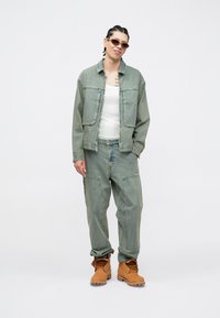 Τζιν μπουφάν και παντελόνι σε ανοιχτό μπλε με άνετη εφαρμογή, συνδυασμένα με ταμπά μπότες. Γυαλιά ηλίου και λευκή αμάνικη μπλούζα ολοκληρώνουν το σύνολο.