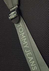Black mesh material with a green strap featuring "TOMMY JEANS" embossed. The strap has a plastic buckle for adjustment.