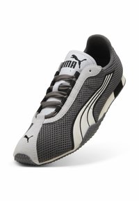 Zapatilla Puma gris y blanca con logo negro, parte superior de malla, cordones y suela texturizada en ángulo sobre fondo blanco.