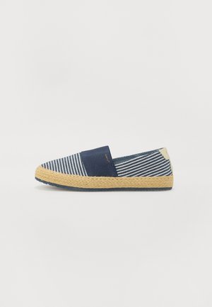 Chaussure sans lacets rayée bleu et blanc avec semelle beige tissée et bande élastique bleu marine sur le dessus sur fond blanc uni.