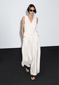 Vitt linne jumpsuit med V-ringning, omslagsdesign och vida ben. Parat med svarta sandaletter med remmar och mörka solglasögon. Minimalistisk stil.