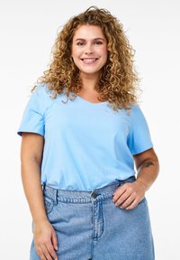 T-shirt azzurro chiaro con scollo a V e maniche corte, realizzato in tessuto morbido. Indossato con una gonna in denim chiaro a vita alta.