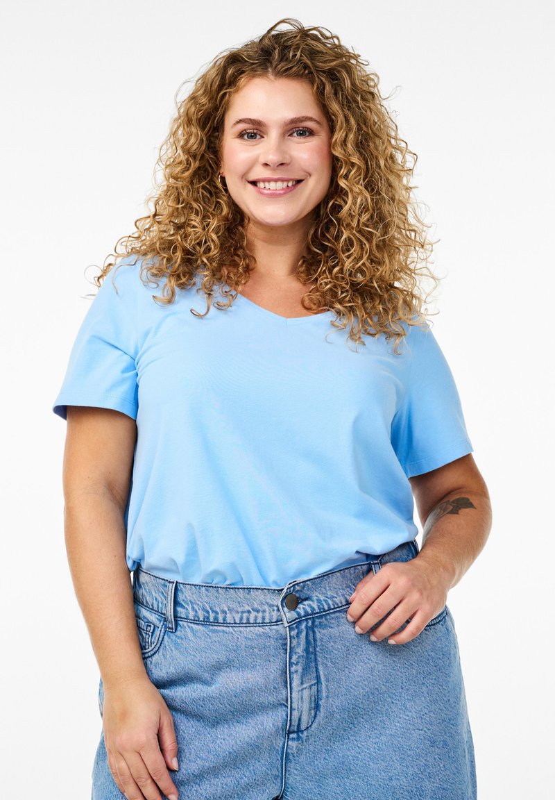 T-shirt azzurro chiaro con scollo a V e maniche corte, realizzato in tessuto morbido. Indossato con una gonna in denim chiaro a vita alta.