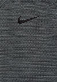 Haut de sport gris foncé en tissu texturé avec un motif rayé subtil. Un logo Nike noir est positionné sur la poitrine.