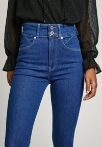 Μπλε τζιν παντελόνι ψηλής μέσης με κλείσιμο δύο κουμπιών, μπροστινές τσέπες και αντίθετη ραφή; λεία υφή χωρίς ορατές φθορές.