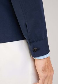 Granatowa koszula z długim rękawem, z mankietem zapinanym na guziki i etykietą "Modna", wykonana z gładkiej bawełny z kontrastowym jasnoniebieskim kołnierzykiem.