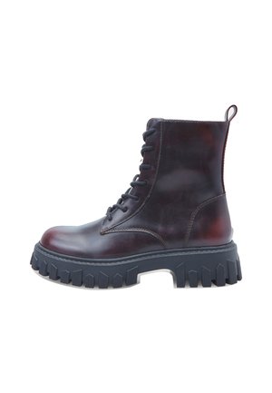 Tumši brūni ādas kaujas zābaki ar biezu melnu profilu un melnām saitēm, skatīti no sāniem uz baltā fona.