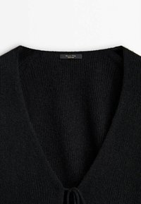Pull noir en maille à col en V avec un petit nœud à l'avant et une étiquette "Massimo Dutti" à l'intérieur du col.
