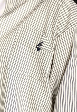 Camisa a rayas en blanco y azul marino, con un diseño de botón. Bolsillo en el pecho izquierdo, con un detalle de logo bordado encima del bolsillo.