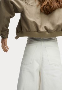 Veste bomber kaki avec un ourlet côtelé et des manches larges, assortie à un pantalon en denim blanc taille haute avec des poches arrière.
