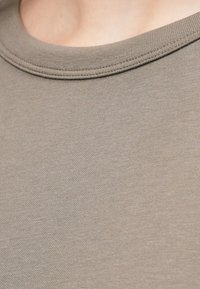 Close-up of a light brown crew neck T-shirt fabric showing fine knit texture and stitching detail along the neckline.