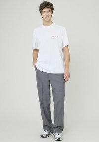 T-shirt en coton blanc avec du texte rouge sur la poitrine, associé à un pantalon gris et des chaussures de sport argentées. Design simple et coupe décontractée.