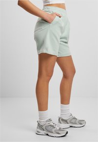 Light green cotton shorts with an elastic waistband, side pockets, and a relaxed fit, paired with gray athletic shoes and white socks.