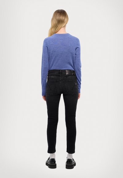 Pull en tricot bleu à manches longues, associé à un jean noir taille haute. Chaussures noires à semelles épaisses. Modèle vu de dos.