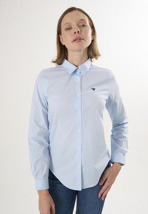 Chemise bleu clair à col, en tissu doux, ornée d'un petit logo d'oiseau marine sur la poitrine gauche et à manches longues.
