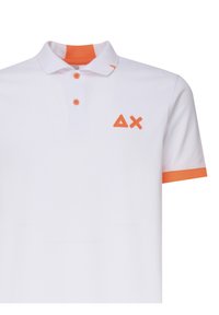 Polo bianco con accenti arancioni, dotato di colletto, due bottoni e un logo triangolare. Tessuto liscio, design classico.