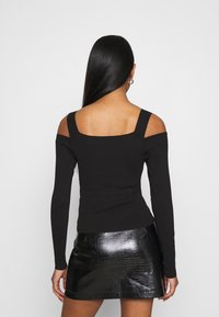 Schwarzes Off-Shoulder-Oberteil mit langen Ärmeln, gerippter Textur und quadratischer Ausschnitt, kombiniert mit einem schwarzen, glänzenden Minirock im Krokodil-Muster.