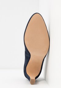 Tossup navy suede korkea kantapää kengät terävä kärki ja sileä vaaleanruskea pohja, jossa on teksturoitu kuvio.