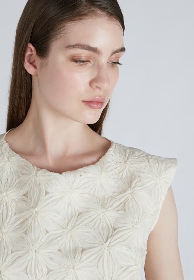 Abito bianco con un motivo floreale a rilievo, design senza maniche e scollatura rotonda con una finitura morbida e trasparente.