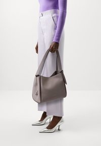 Grijze leren hobo tas met een gladde textuur en schouderband, gecombineerd met lichtpaarse broeken en zilveren hoge hakken.