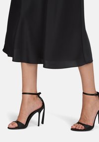 Czarne sandały na wysokim obcasie z otwartym palcem, gładki materiał przypominający satynę, pasek na kostkę oraz cienki obcas typu stiletto. Prosty i elegancki design.