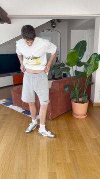 T-shirt branca com impressão "Scent of Summer", calções cinzentos com logotipo preto, sapatilhas de atletismo prateadas e planta de interior em vaso de terracota.