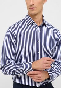 Gestreepte button-up shirt in marineblauw en wit, met een klassieke kraag, lange mouwen en een getailleerd ontwerp. Stof lijkt glad en gestructureerd.