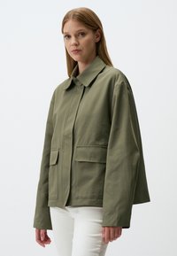 Giacca verde oliva, in cotone, vestibilità comoda, collo a punta, due tasche frontali, chiusura con bottoni, progettata per un abbigliamento informale.