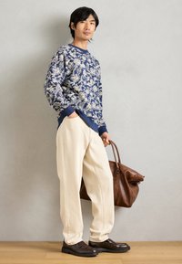 Ναυτικό φούτερ με floral μοτίβο, κρεμ παντελόνι σε φαρδιά γραμμή, καφέ δερμάτινη τσάντα, σκούρα καφέ παπούτσια, άνετη εφαρμογή, λεία υφή υφάσματος.