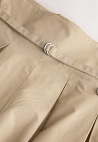 Jupe beige taille haute avec ceinture en tissu avec boucle double anneau argentée et plis.