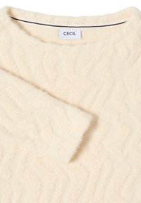 Suéter color crema con un patrón texturizado, hecho de un material suave, con cuello redondo y mangas cortas. Etiqueta de la marca visible.