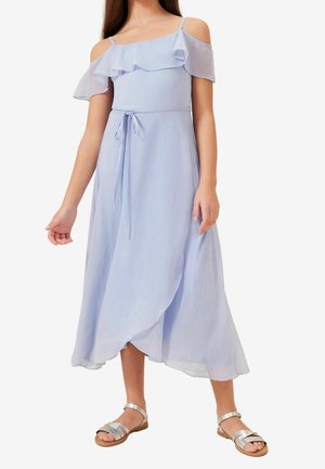 Pige iført en lyseblå off-shoulder midi-kjole med flæsedetaljer og bindebånd i taljen, stylet med sølvfarvede sandaler på en hvid baggrund.