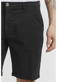 Black cotton shorts with a button closure, front pockets, and a straight cut. The fabric has a smooth texture and minimal stitching details.