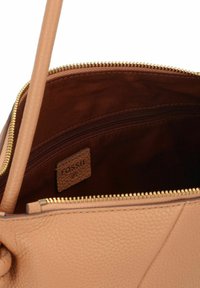 Innenraum einer tanfarbenen Ledertasche mit einem goldenen Reißverschluss, ausgestattet mit einer braunen Stoffauskleidung und einem kleinen braunen Etikett, das "FOSSIL" eingeprägt hat.