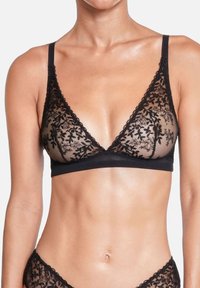 Bralette en dentelle noire avec broderie florale, bonnets souples en forme de triangle, bretelles réglables et bande inférieure lisse. Matière légère et transparente.