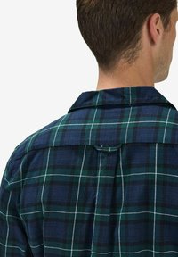 Ruudullinen flanellipaita, jossa on tummanvihreitä ja laivastonsinisiä värejä sekä valkoisia ruutulinjoja. Paidassa on terävä kaulus ja keskellä pleat-yksityiskohta takana.