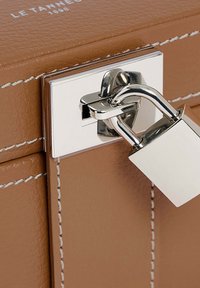 Caja de cuero marrón con costuras blancas, que presenta un pestillo metálico y herrajes plateados, exhibiendo un diseño elegante y estructurado.