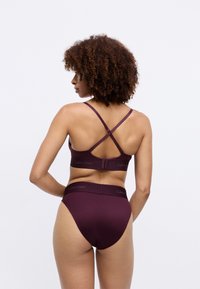 Set de sutien maron și chiloți cu talie înaltă, confecționat dintr-un material neted. Prezintă bretele încrucișate și un elastic cu marcă la talie.