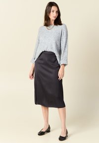 Maglione azzurro chiaro in tessuto strutturato, gonna midi nera in satin e scarpe nere con tacco a blocco in vernice. Collana a catena bianca ben visibile. Design semplice ed elegante.