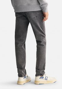 Szare dżinsy o prostym kroju, z tylnymi kieszeniami i delikatnym efektownym sfatygowaniem. Połączone z jasnymi trampkami.