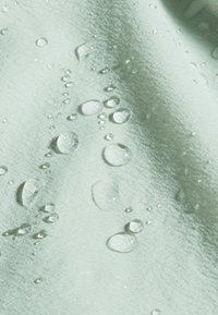 Tessuto verde menta con una texture morbida, caratterizzato da molteplici gocce d'acqua sulla superficie, che evidenziano le sue proprietà resistenti all'acqua.