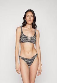 Bikini set v camo vzoru, který obsahuje bralet v čtvercovém výstřihu s kulatým kovovým akcentem a dolní část s nízkým pasem a tenkými ramínky v šedé a zelené barvě.