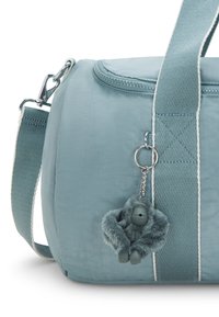 Teal stof duffel tas med lynlåsåbning, med en tekstureret rem og en grå fluffy gorilla nøglering hængende som dekoration.