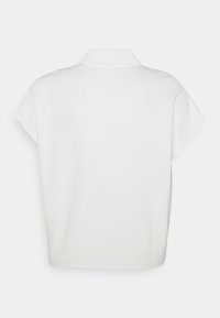 Weißes Polo-Shirt mit kurzen Ärmeln, leicht gerundetem Kragen und lockerer Passform. Glatte Stoffoberfläche ohne sichtbare Muster oder Hardware.