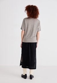Grijze korte mouw shirt gecombineerd met een zwarte maxi rok met zijsplits, gedragen over crèmekleurige broek en zwarte schoenen.