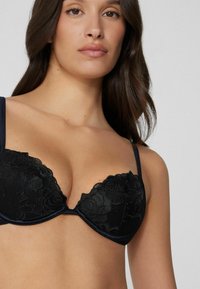 Schwarzer Spitzen-BH mit floralem Muster, vorgeformten Cups und Satin-Trägern. Verfügt über eine glatte Oberfläche und ein tiefes Dekolleté-Design.